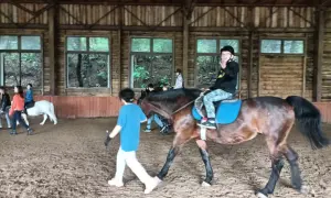 W stajni Black Horse Team Gdańsk, w owczarni, chłopiec na koniu macha do widza, a obok niego idzie instruktorka.