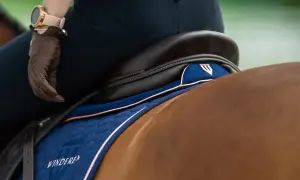 Jeździec w brązowej rękawiczce i zegarku siedzi na koniu. Pod siodłem widać granatową podkładkę żelową pod siodło z różowymi lamówkami.