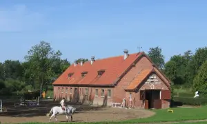 Jazda konna na tle ceglanej stajni z czerwonym dachem.